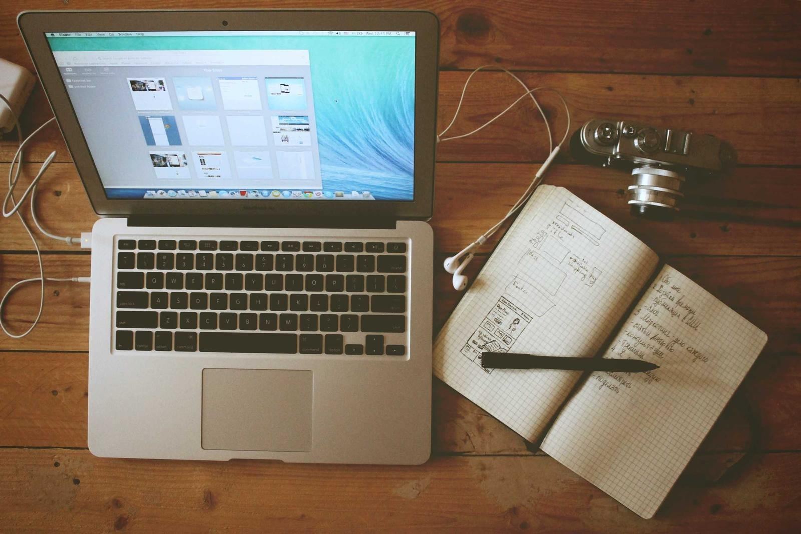 An open laptop and notebook on a wooden desk