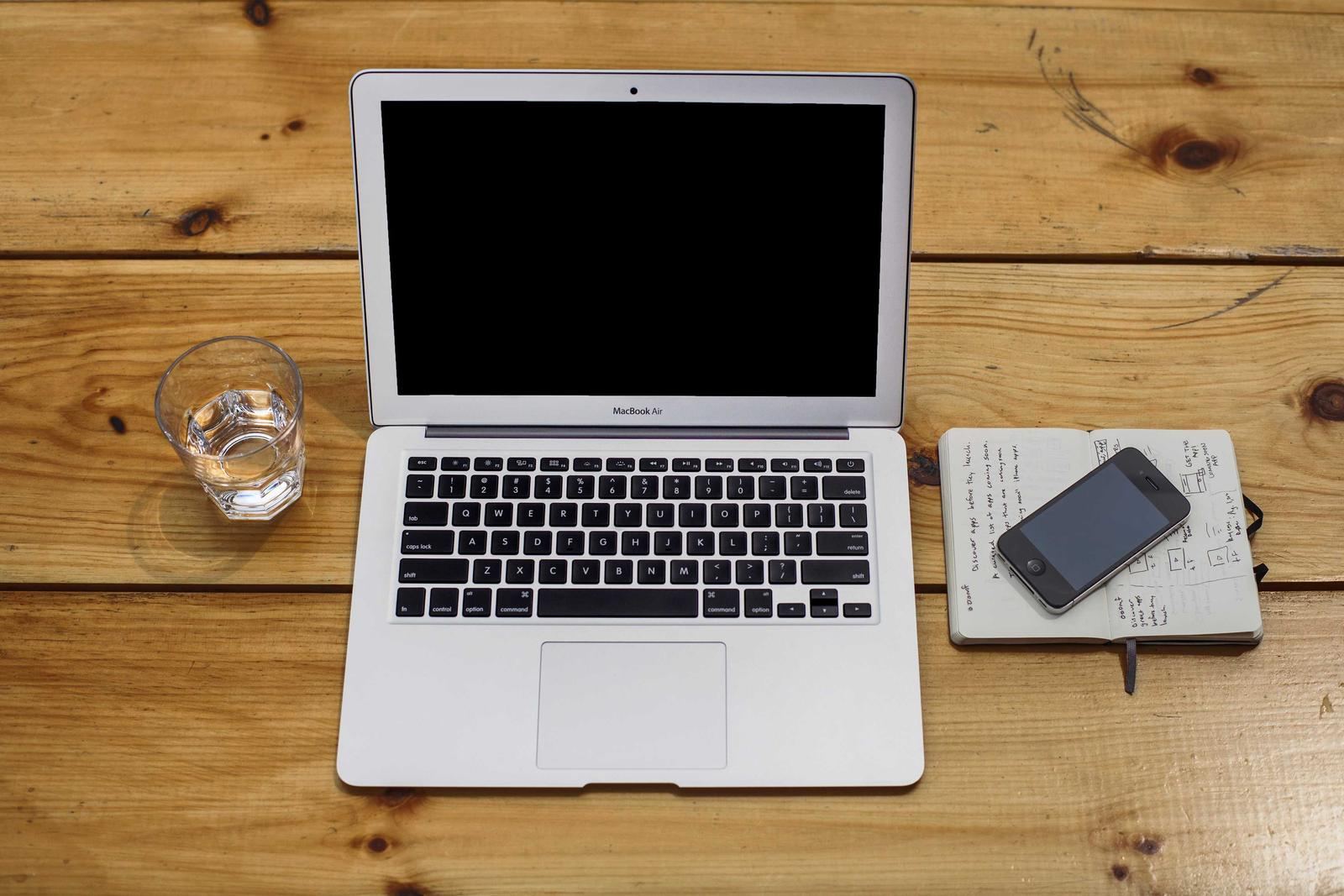 A laptop with a notebook and phone on a wooden desk