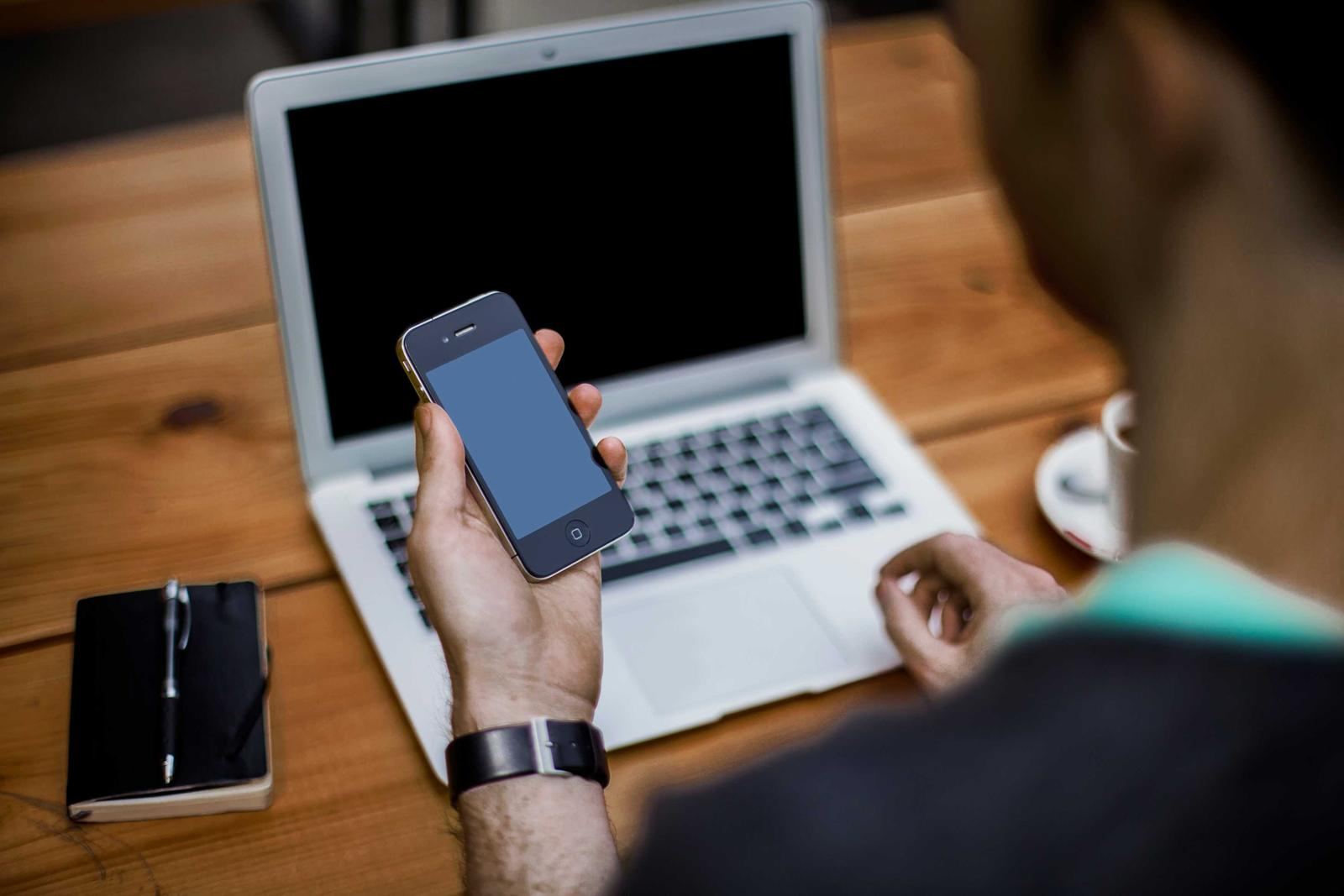 A person using a phone in front of a laptop