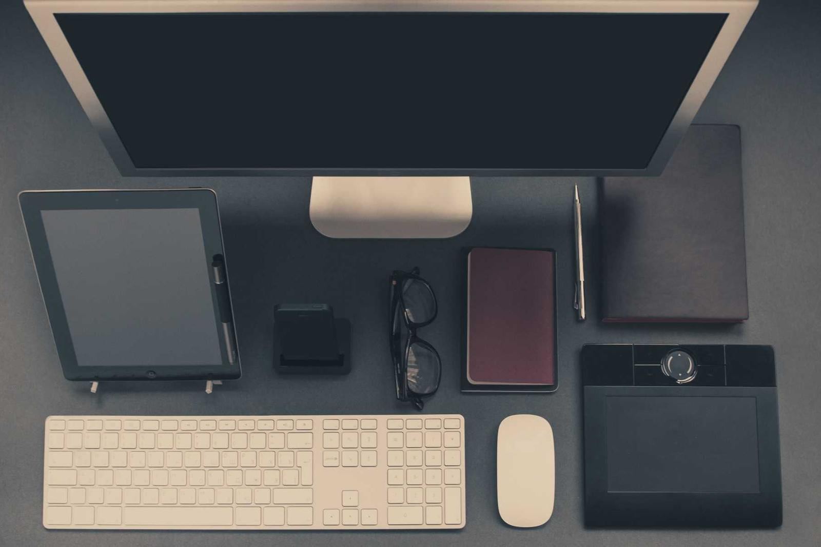 A tidy workstation with a monitor, keyboard, tablet and notebooks